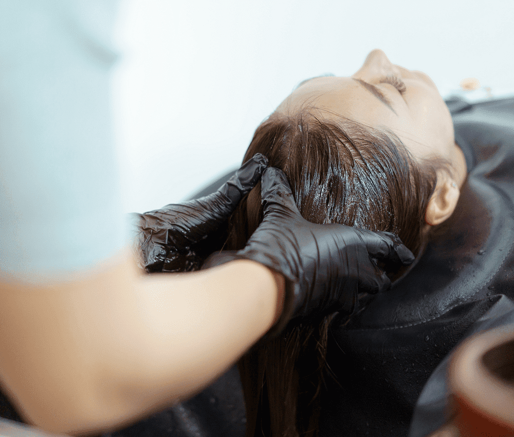 A stylist applies hair dye to a client in a salon.