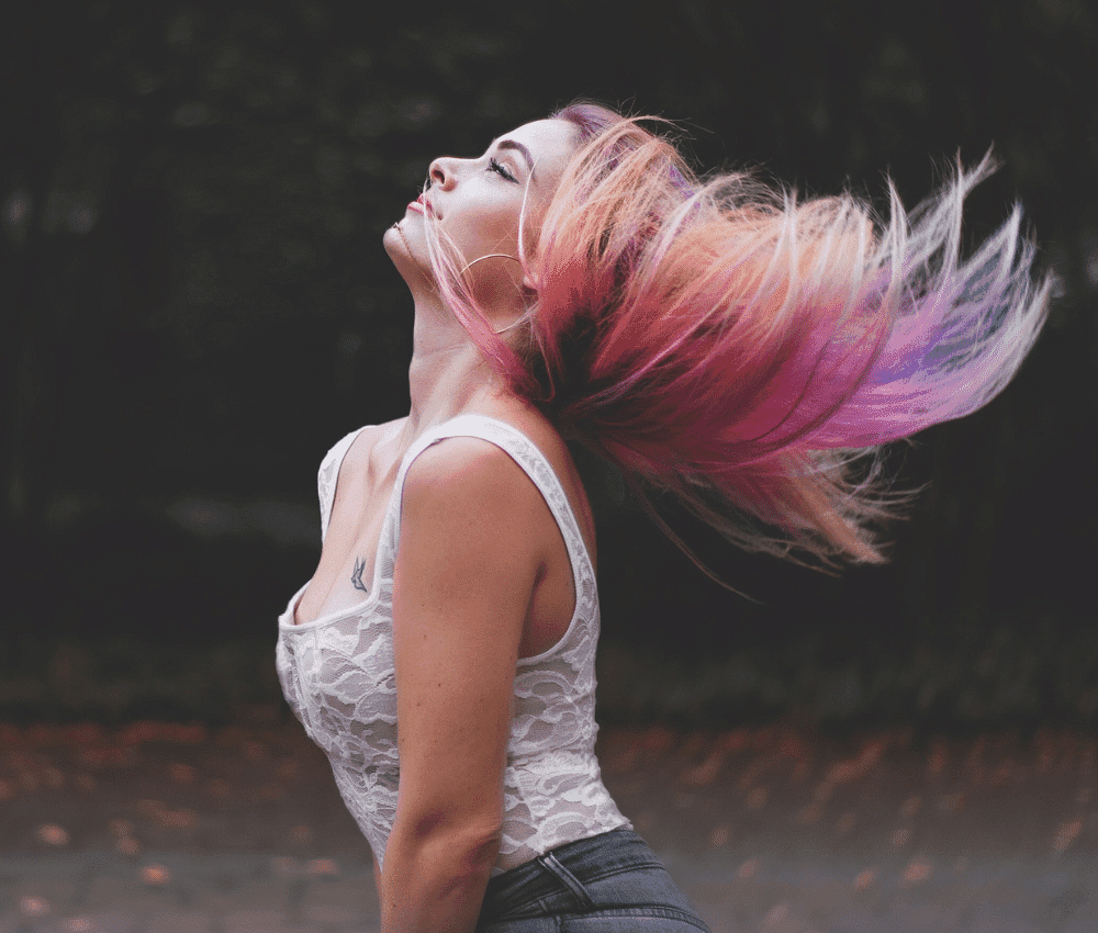 Woman with colorful hair flicking head back outdoors.